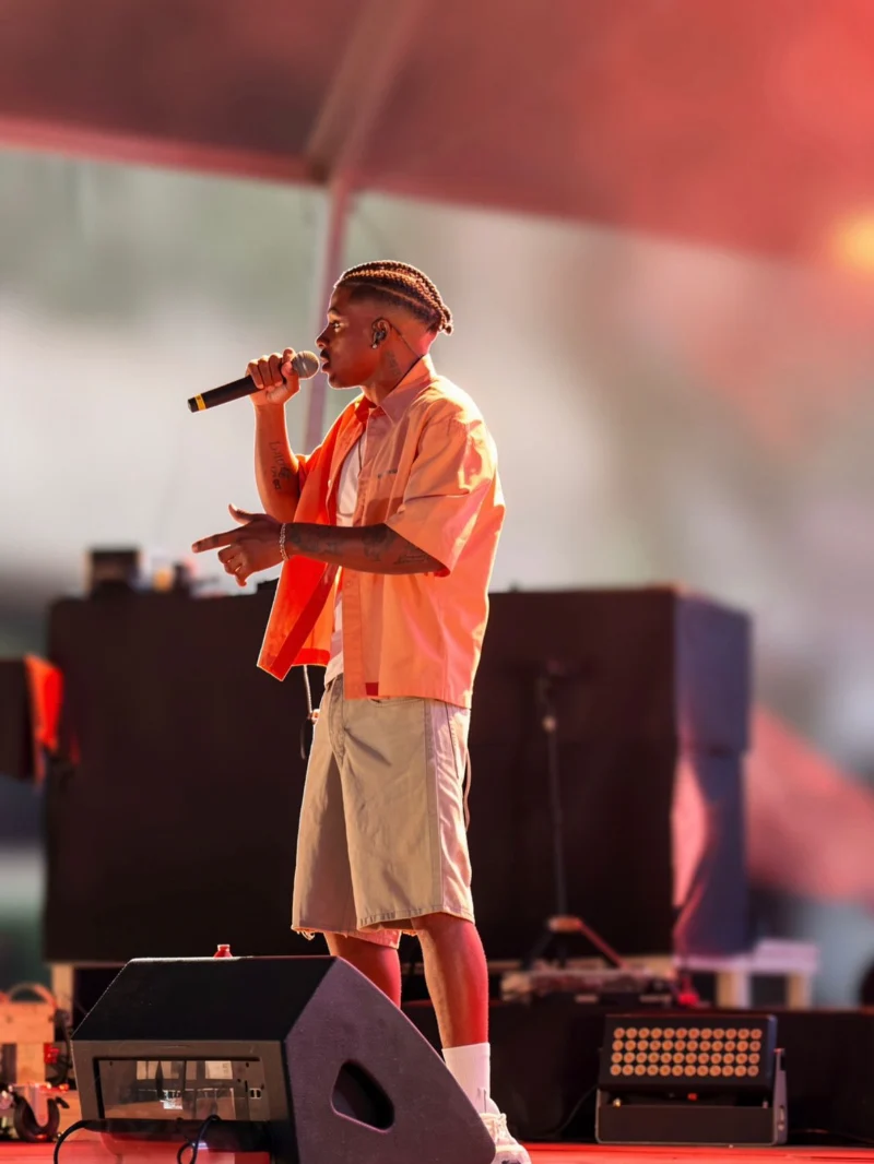 Tungono a cantar de perfil, sob luz âmbar do palco